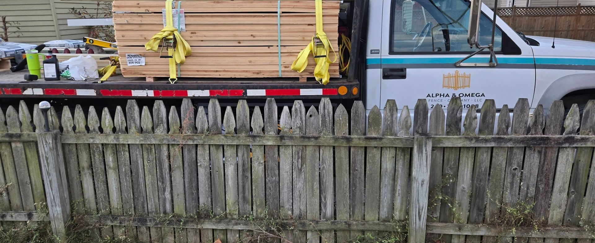 Weathered wooden fence in front of parked trucks with a yellow strap across one truck bed