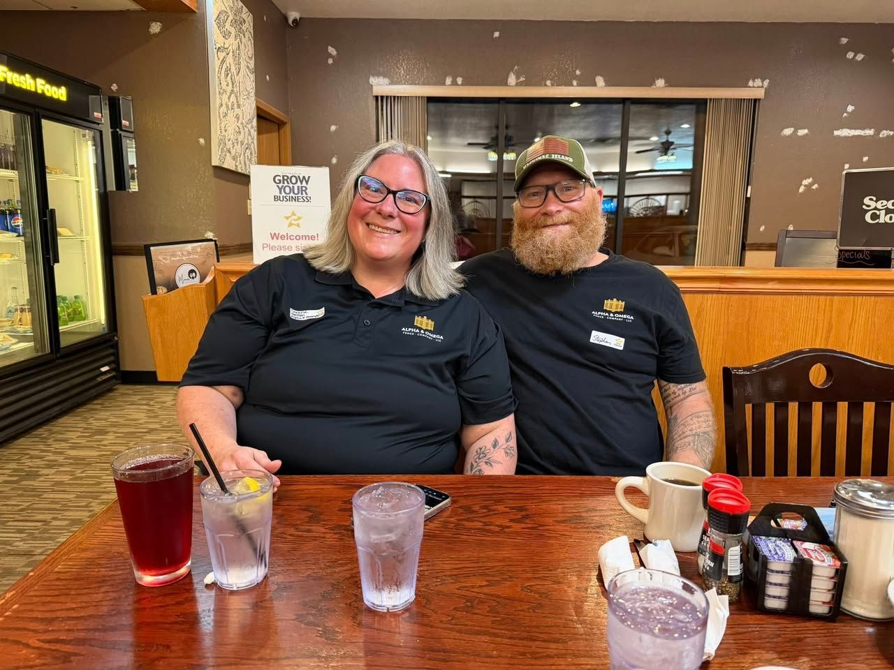 A smiling couple sits at a wooden restaurant table with drinks and condiments in front of them.