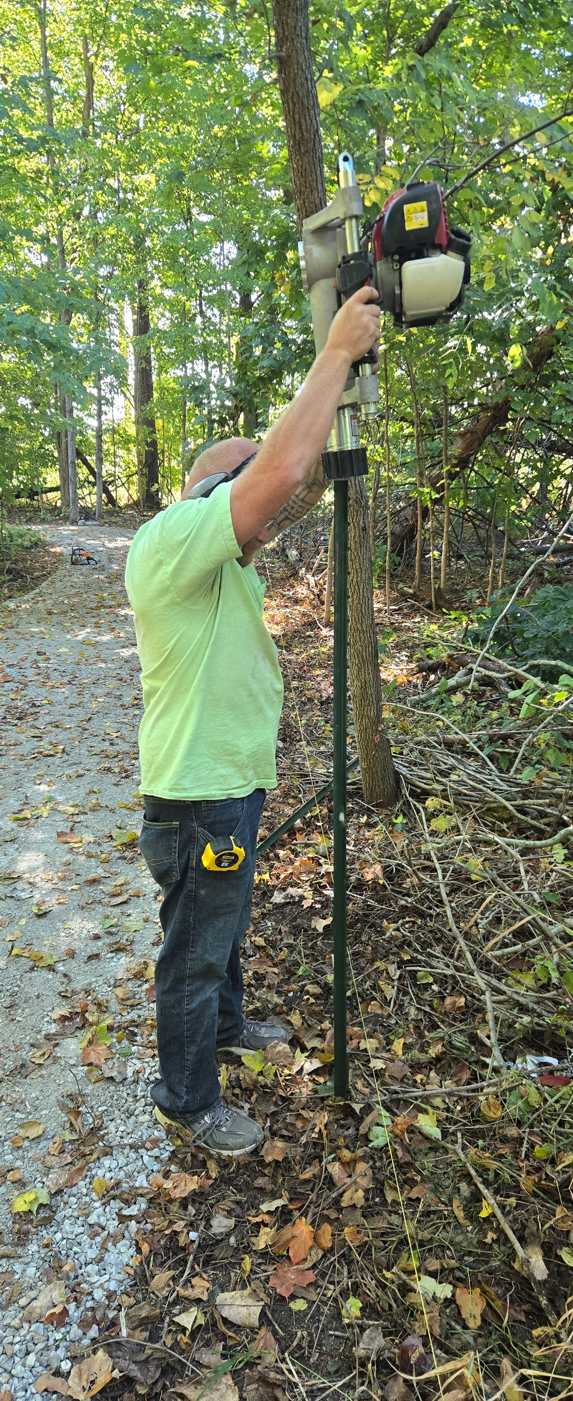 Person in a green shirt reaching up to hang a toy on a tree in a wooded area