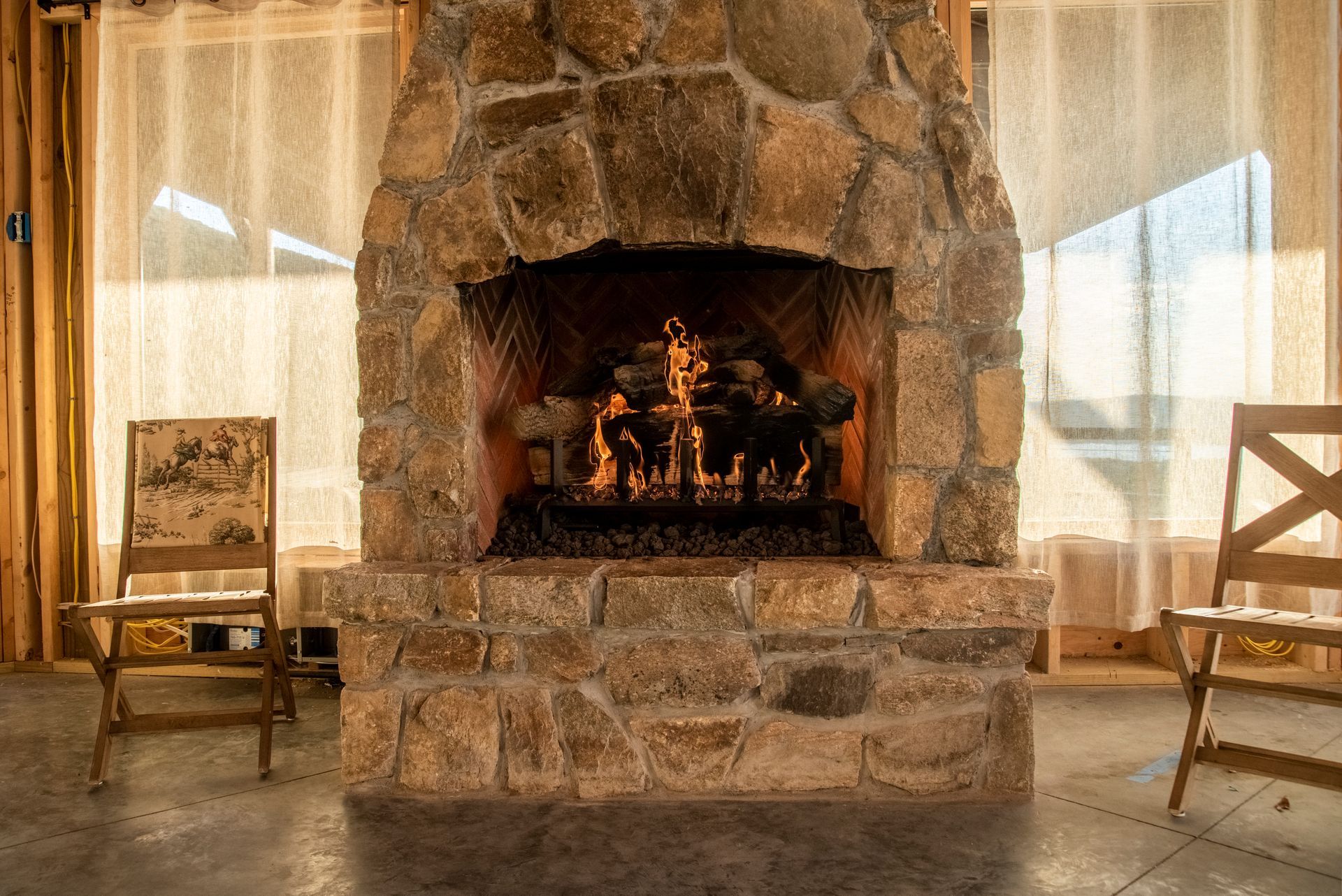 A stone fireplace is sitting in a living room next to two chairs.