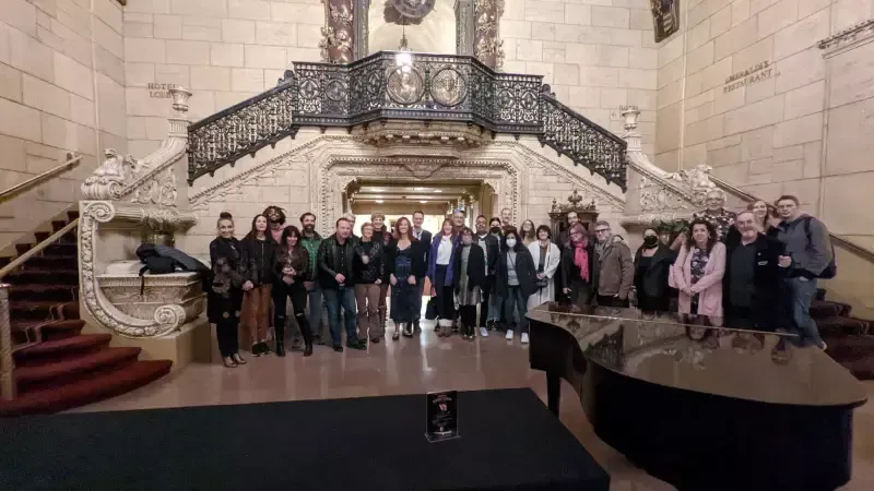 A group of people are posing for a picture in front of a piano and stairs.