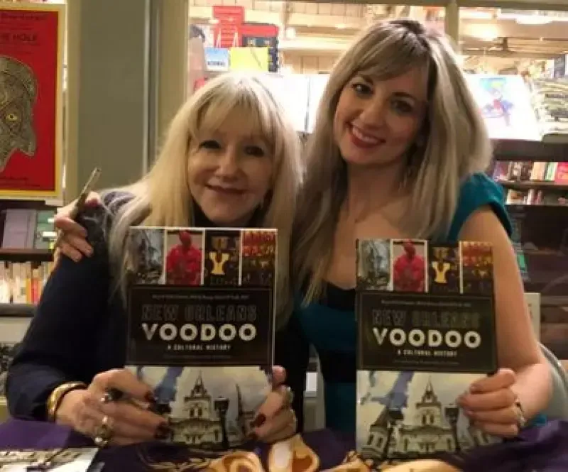 Two women holding a book titled new orleans voodoo