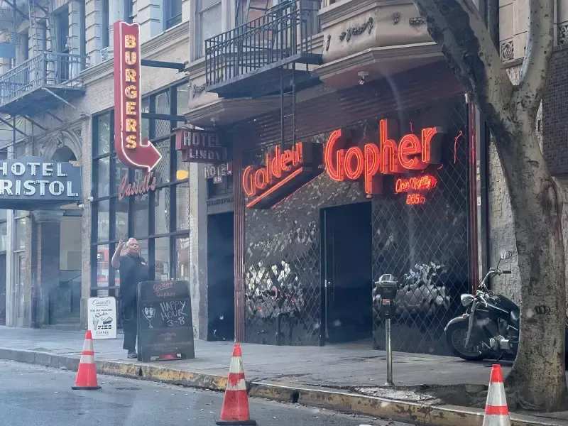A man walking down a street in front of a restaurant called golden gopher