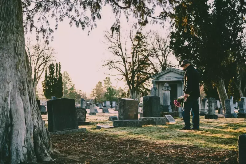 A man is standing in a cemetery holding a flower.