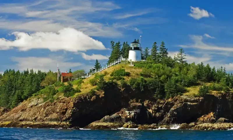Lighthouse on a green, rocky island under a blue sky with white clouds.