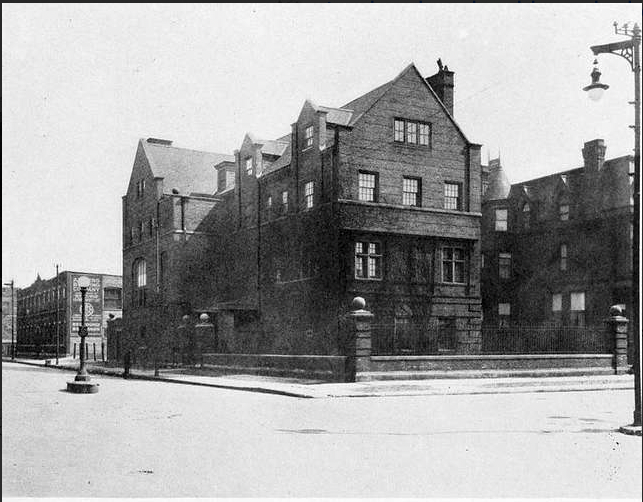 Brick building on a corner, early 20th century, with wrought iron fence and street lamp.