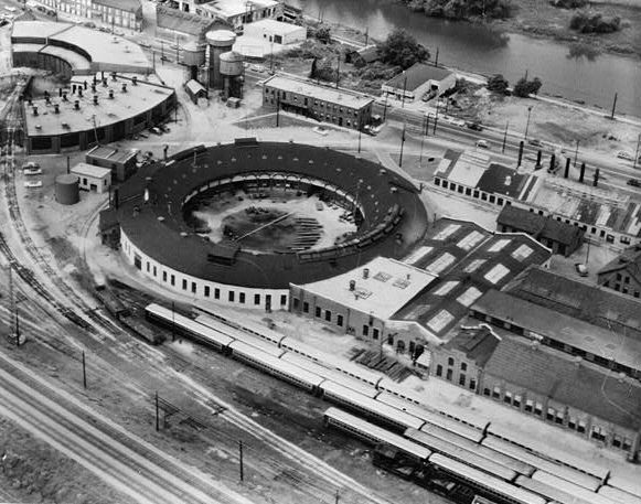 Aerial view of a historic roundhouse and train depot. Trains are parked on tracks.