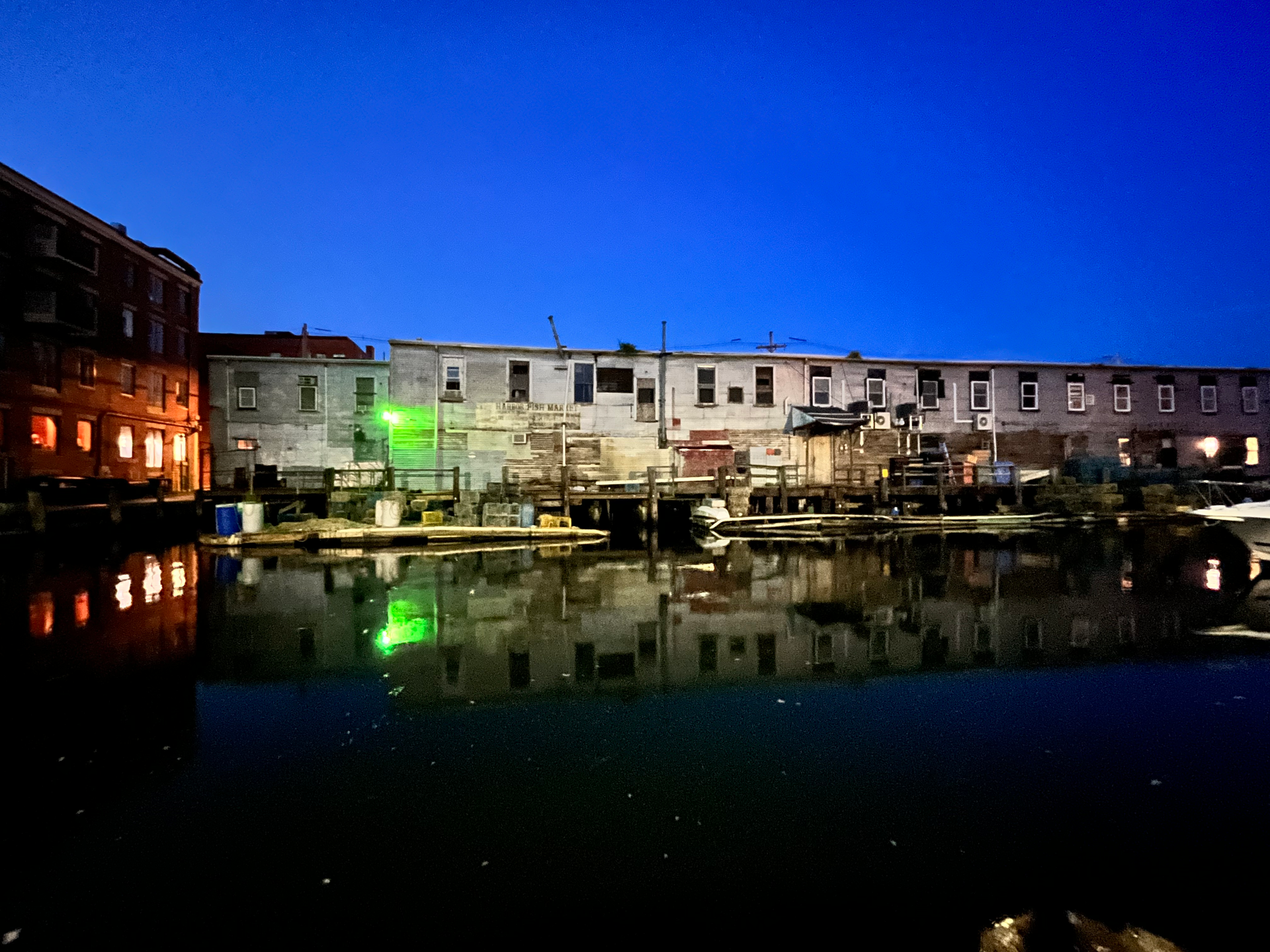 Night view of a canal with reflections of buildings lit with warm and cool tones, under a deep blue sky.