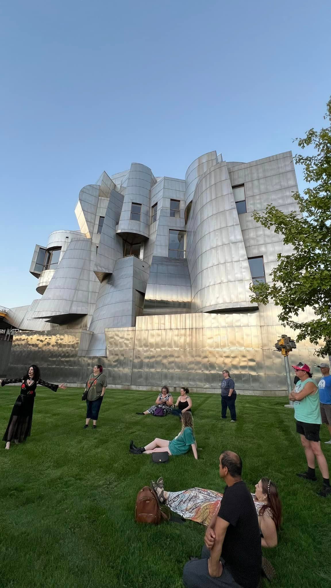 A group of people are sitting in the grass in front of a large building.