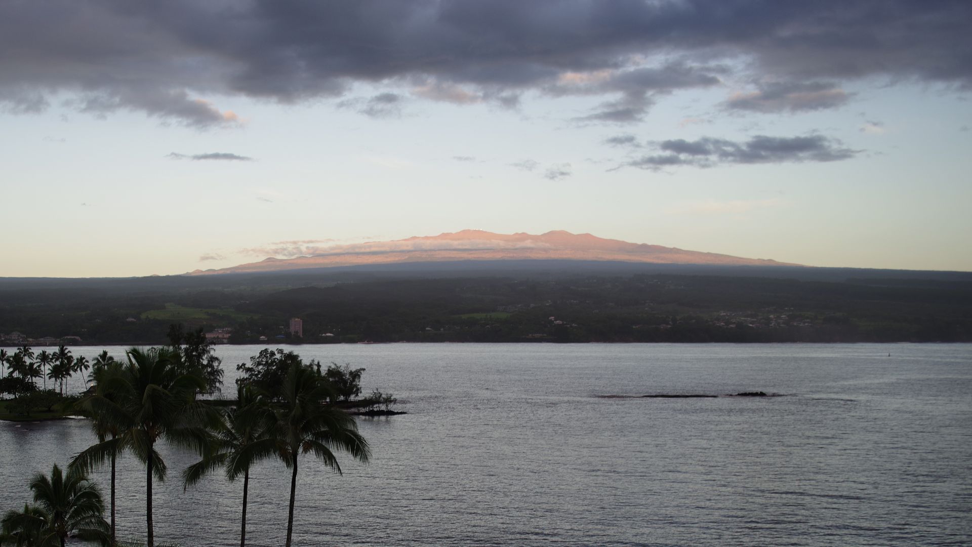 A sunset over a large body of water with palm trees in the foreground.