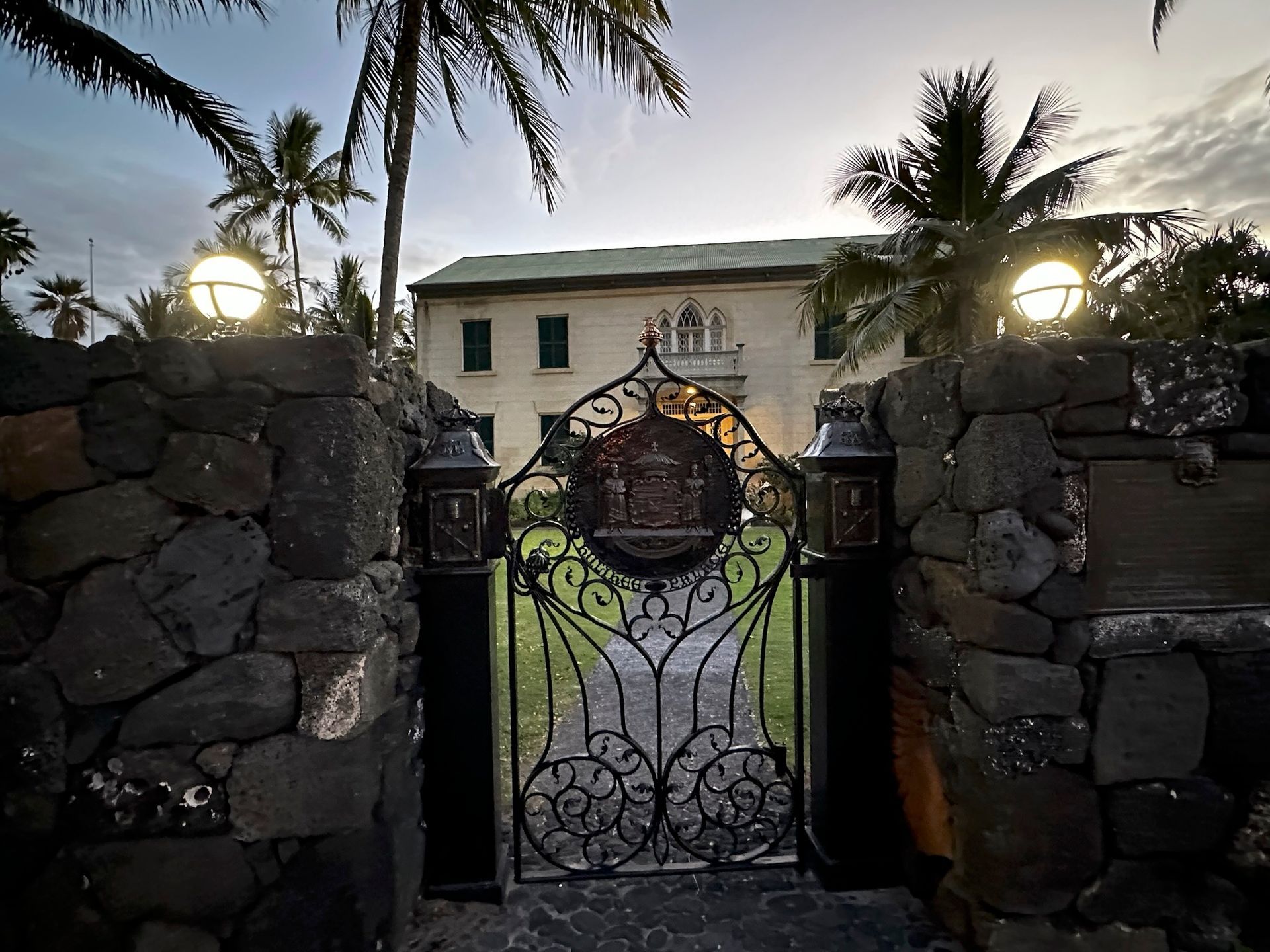 A stone wall with a wrought iron gate leading to a large building