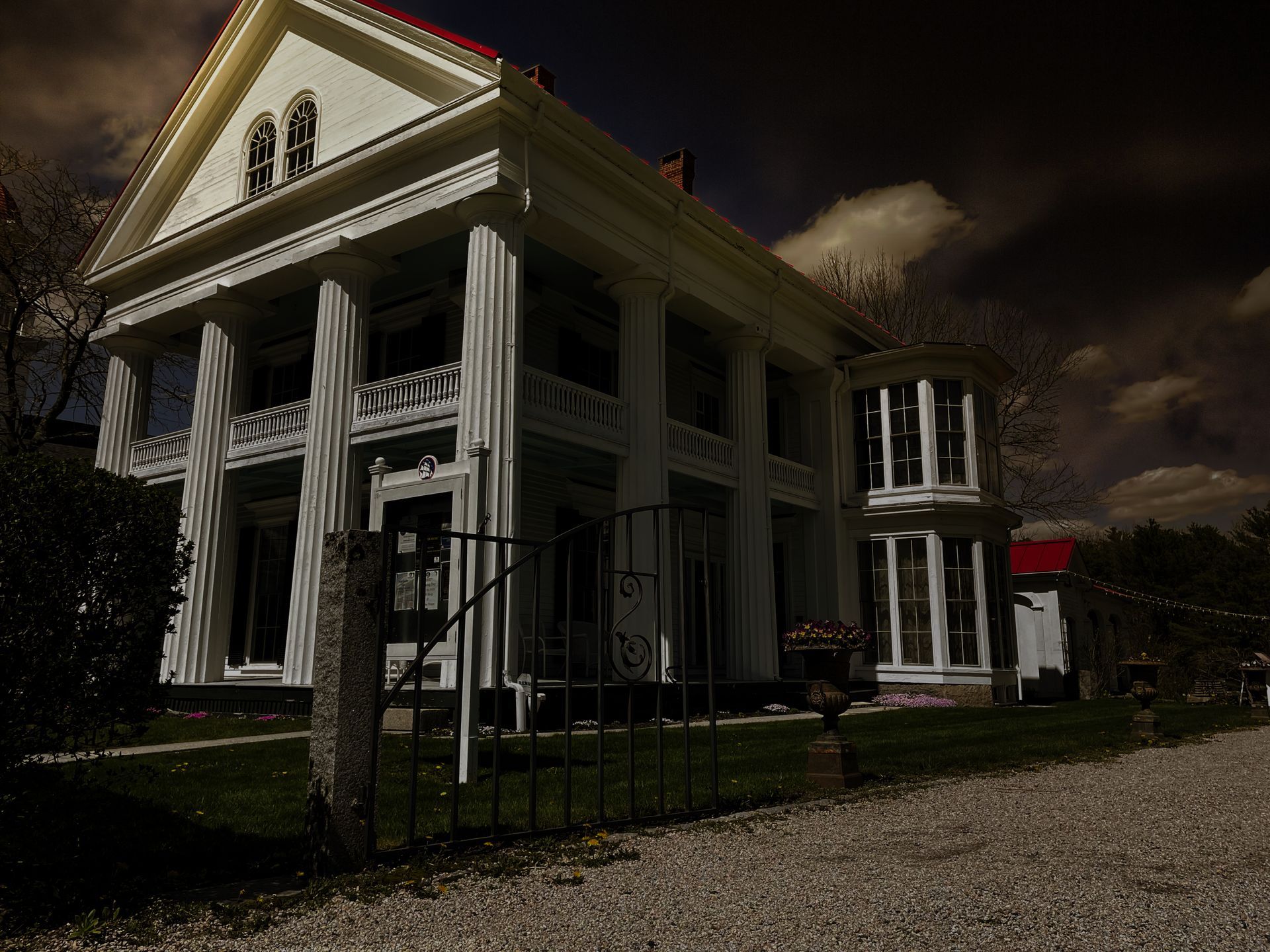Grand white mansion with columns and a turret, framed by a wrought iron fence, against a cloudy sky.