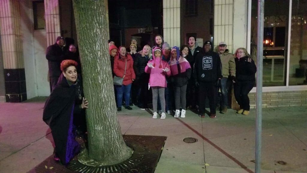 A group of people standing in front of a building with a tree in the foreground