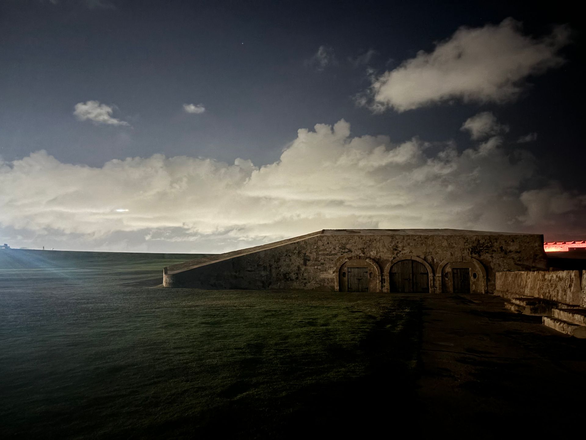 Stone building at dusk with steps, arched doorways, and a cloudy sky.
