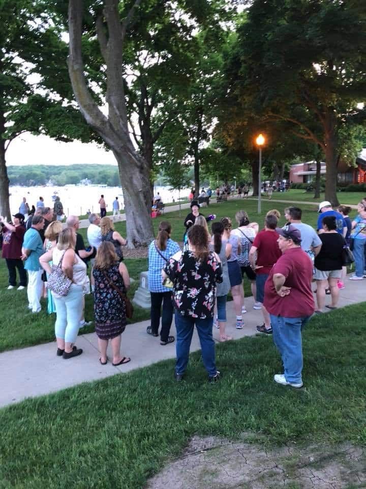 A group of people are standing on a sidewalk near a lake.