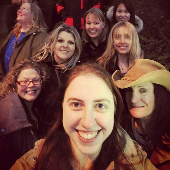 Group of smiling women taking a selfie outdoors at night. One wears a cowboy hat.