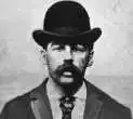 Man with a large mustache, bowler hat, and suit, looking directly at the viewer.