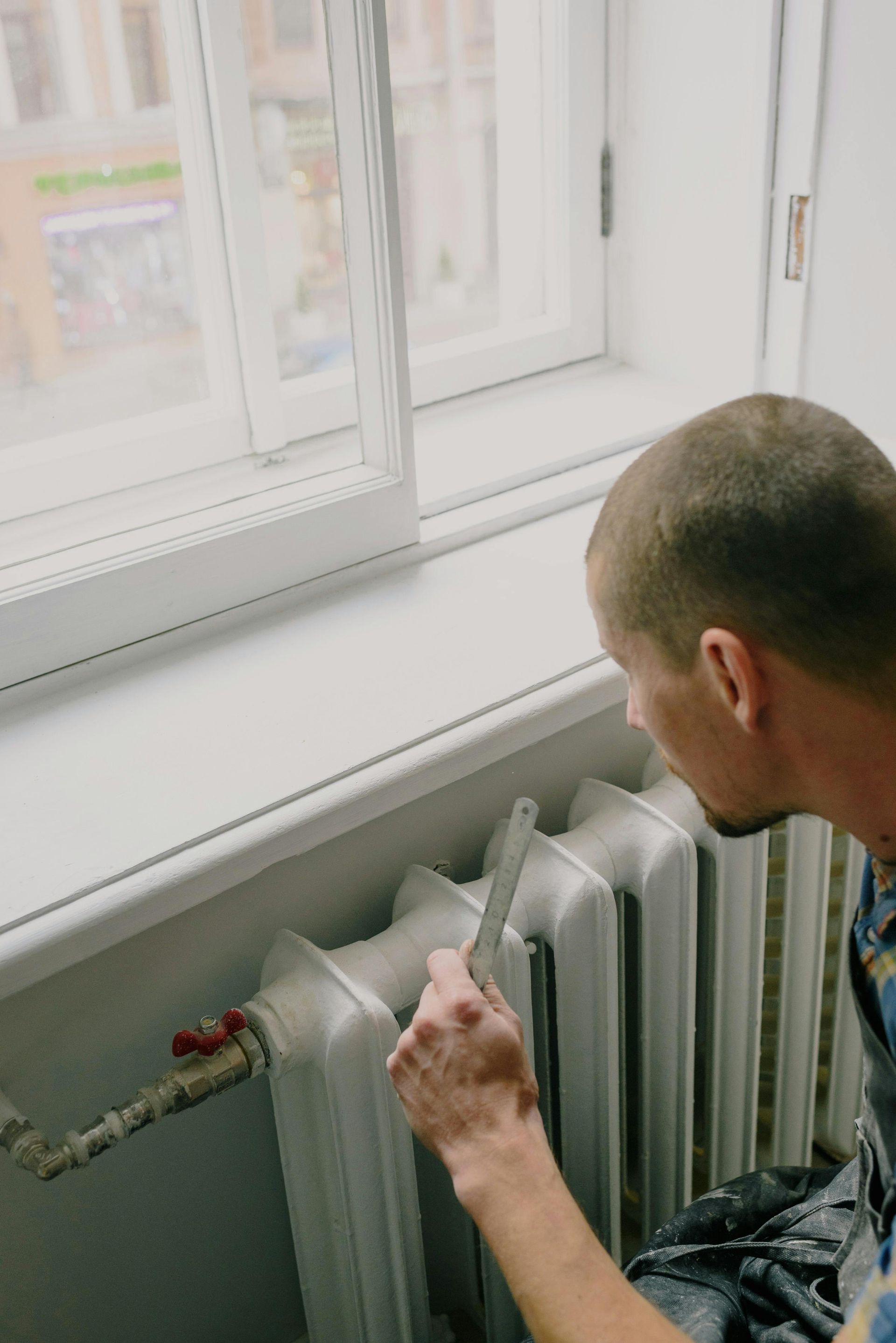 A man is painting a radiator in a room next to a window.