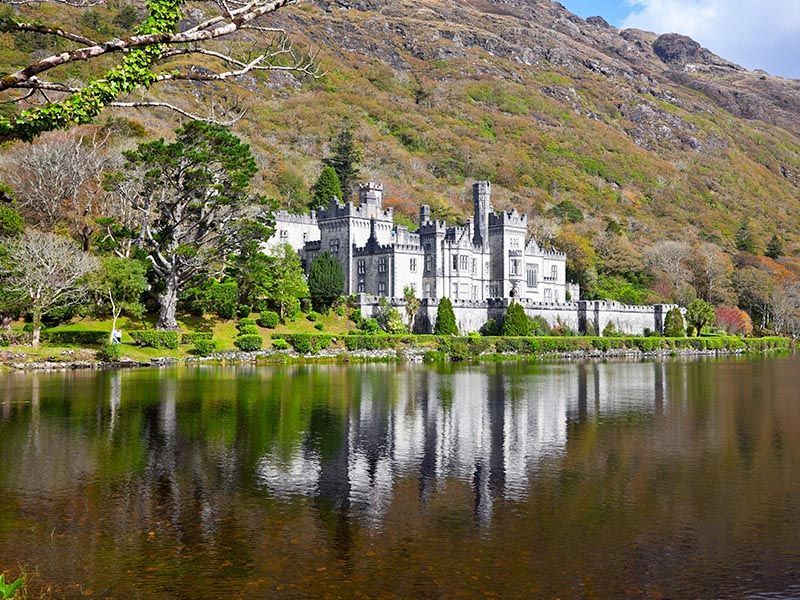 Un grand château dont on voit le reflet dans l'eau entouré de montagne