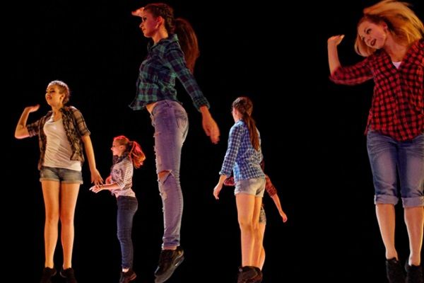 Des jeunes filles en jean font un spectacle de danse sur une scène sur un fond noir
