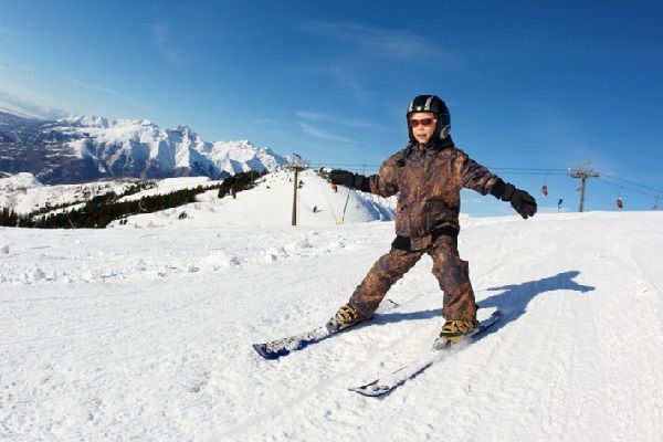 Un enfant se tient debout sur ses skis avec la montagne et le ciel en fond