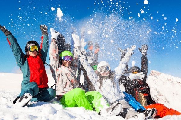 Un groupe d'enfants en combinaison de ski assis dans la neige lève les bras en l'air en jetant de la neige