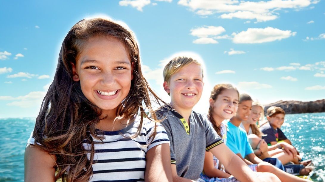 De jeunes enfants posent avec le sourire avec la mer et un ciel bleu en fond