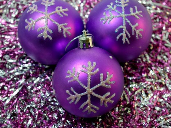 Trois boules d'un sapin de Noël violettes avec un flocon de neige argenté sur un fond de guirlandes violettes