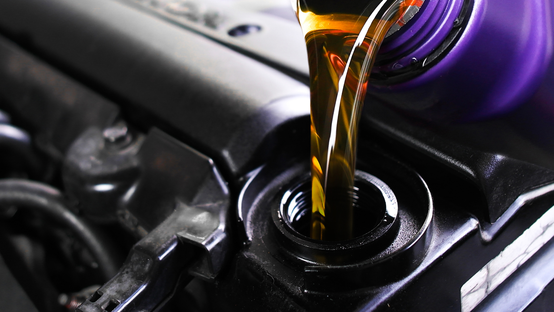 Oil being poured from a purple bottle into a car engine.