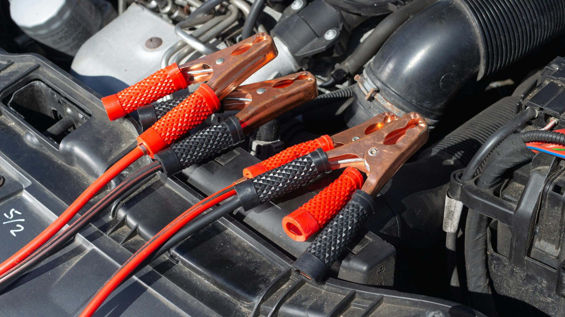 Jumper cables connected to car battery terminals; red and black cables with copper clamps.
