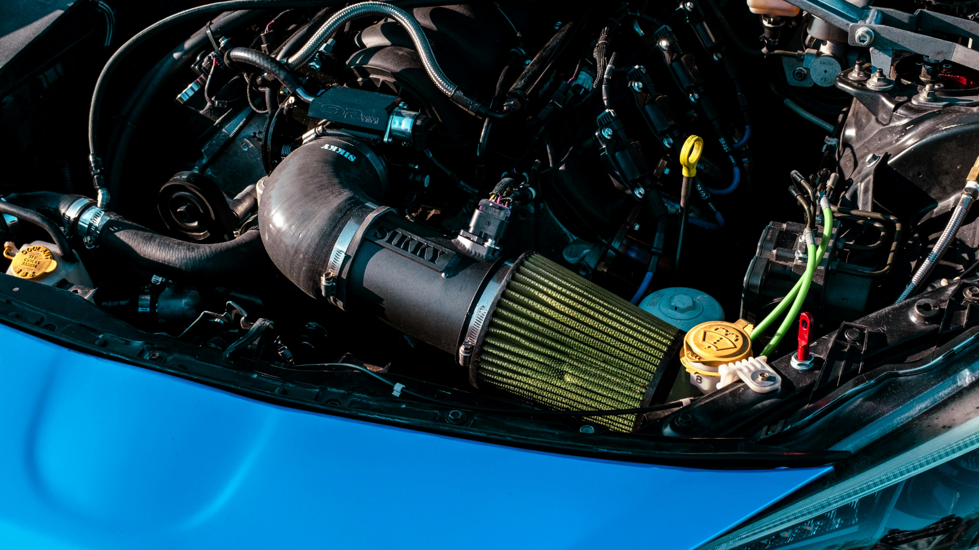 Blue car engine with a black air intake and yellow filter.