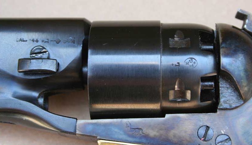 Close-up of a black antique revolver's cylinder and barrel. Markings on the barrel indicate caliber.