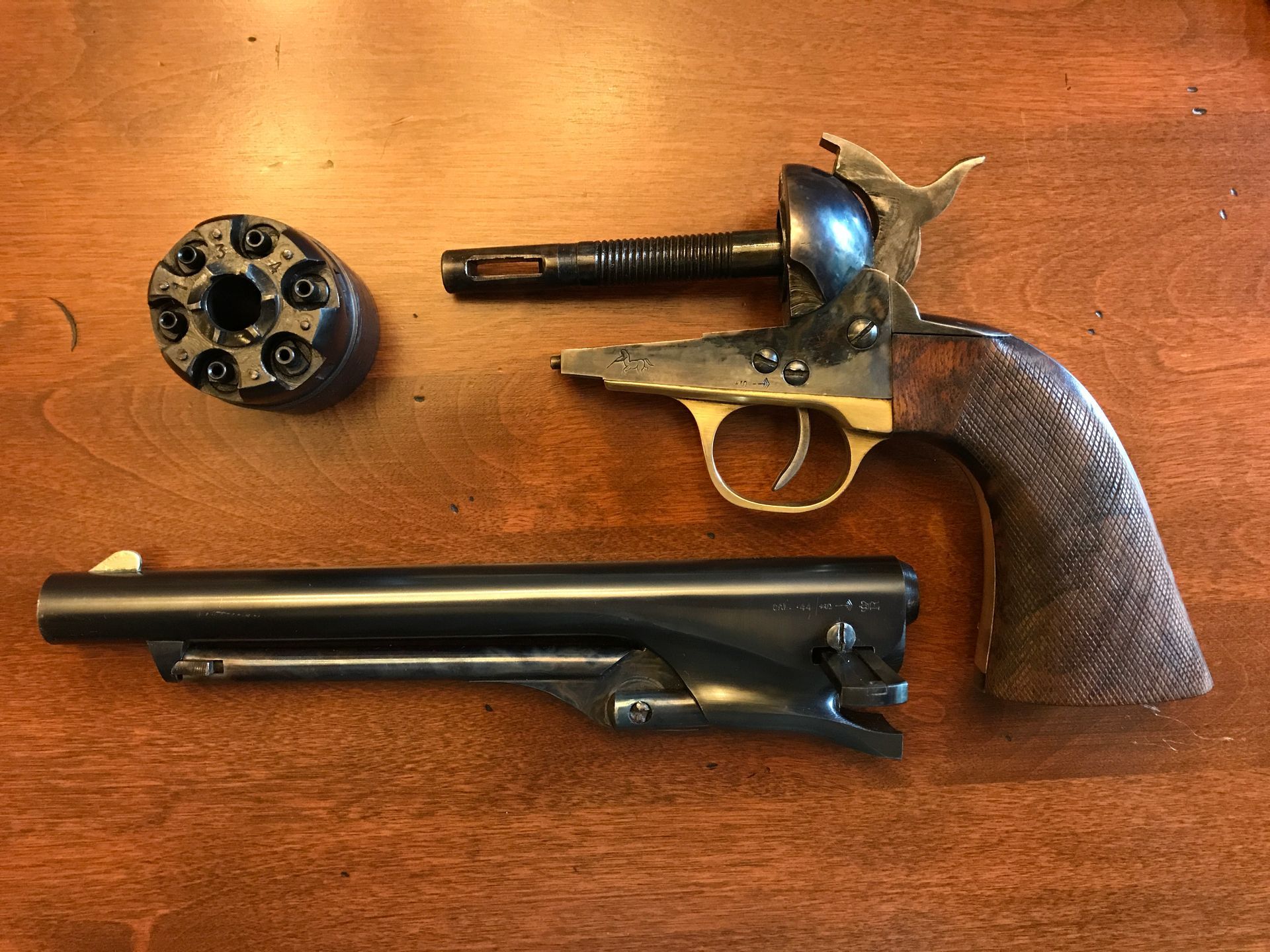 Disassembled antique revolver on a wooden surface, showing barrel, cylinder, and frame.