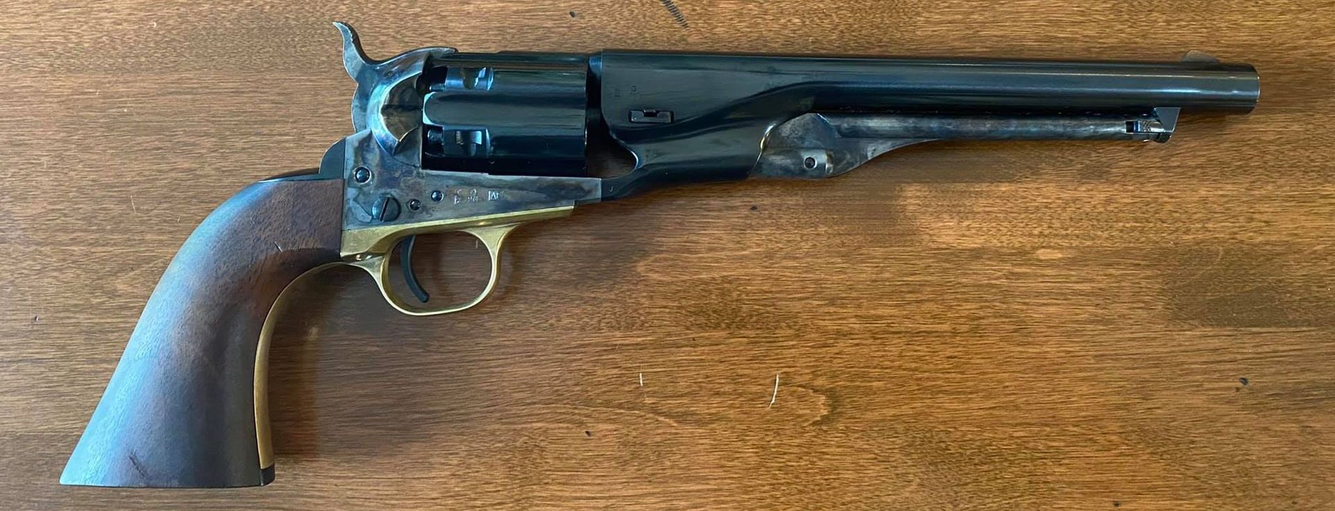 Black and gold antique revolver with wooden grip on a wooden surface.