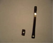 Two small, black main springs with holes; one rectangular, one long and thin, on a light surface.