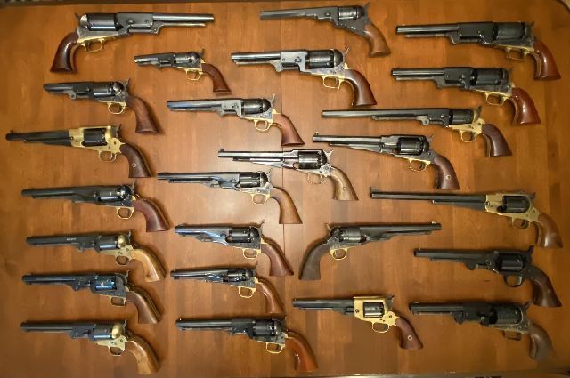 Collection of antique revolvers on a wooden surface, various sizes and finishes displayed.