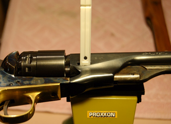 Black revolver with gold accents being measured with a white tool.