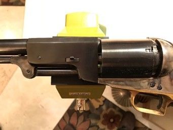 A black and brass antique revolver with a yellow and green device attached, on a light-colored surface.