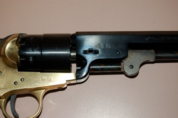 Close-up of a black and brass antique revolver with its cylinder exposed.