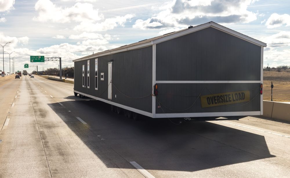 Dark gray tiny house-style trailer parked on a roadside under a cloudy sky