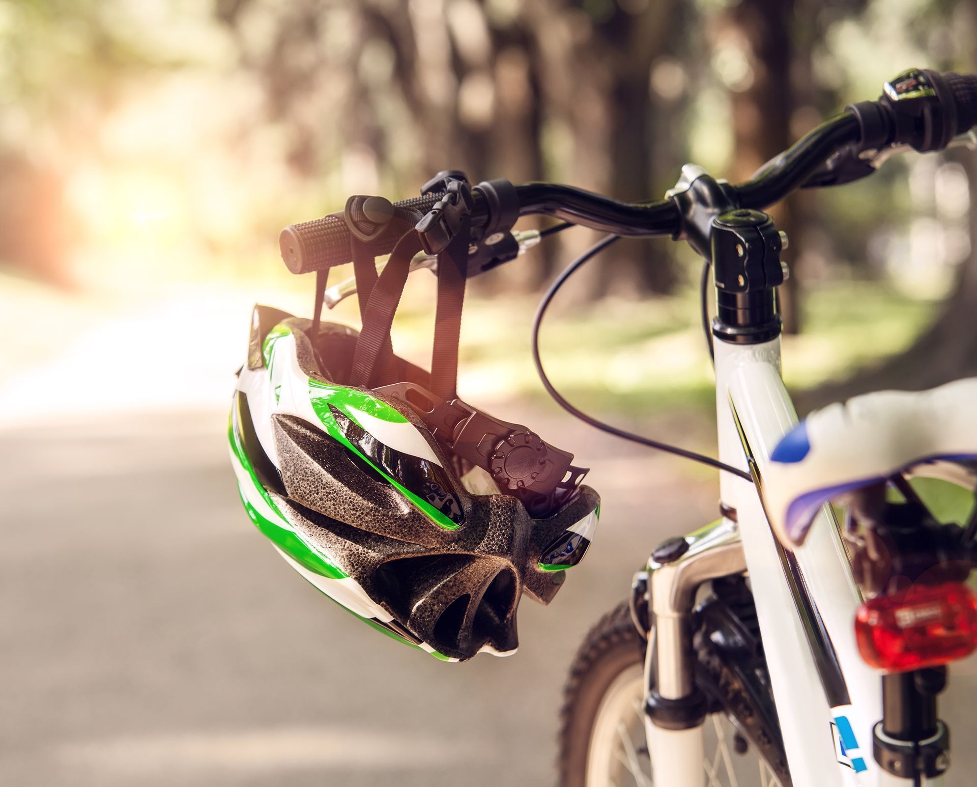 Manubrio di bicicletta con un casco verde e bianco appeso, in un parco.