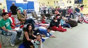 People gathered indoors, some seated in chairs, others on mats.