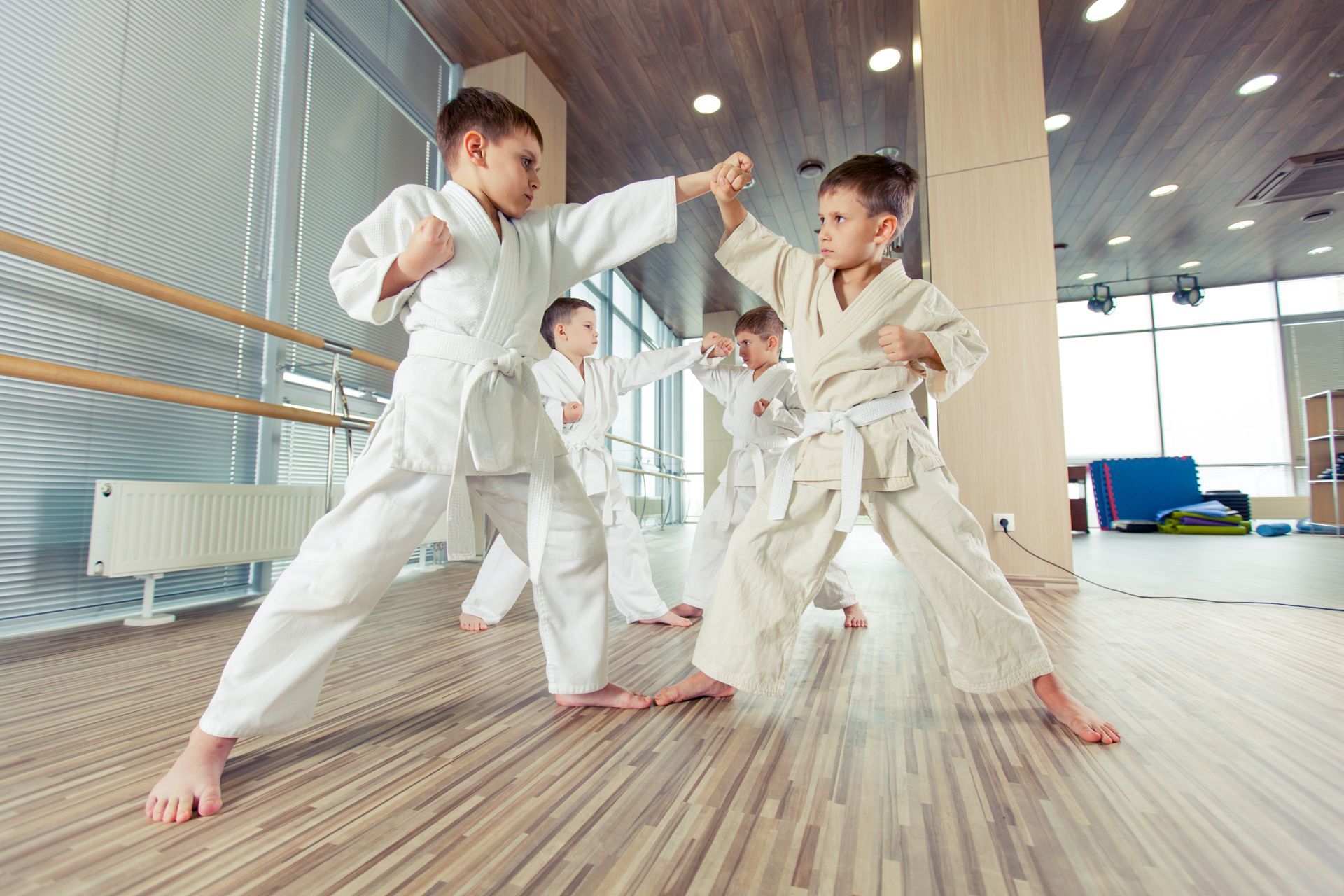 Kids in white karate uniforms practicing in a gym.