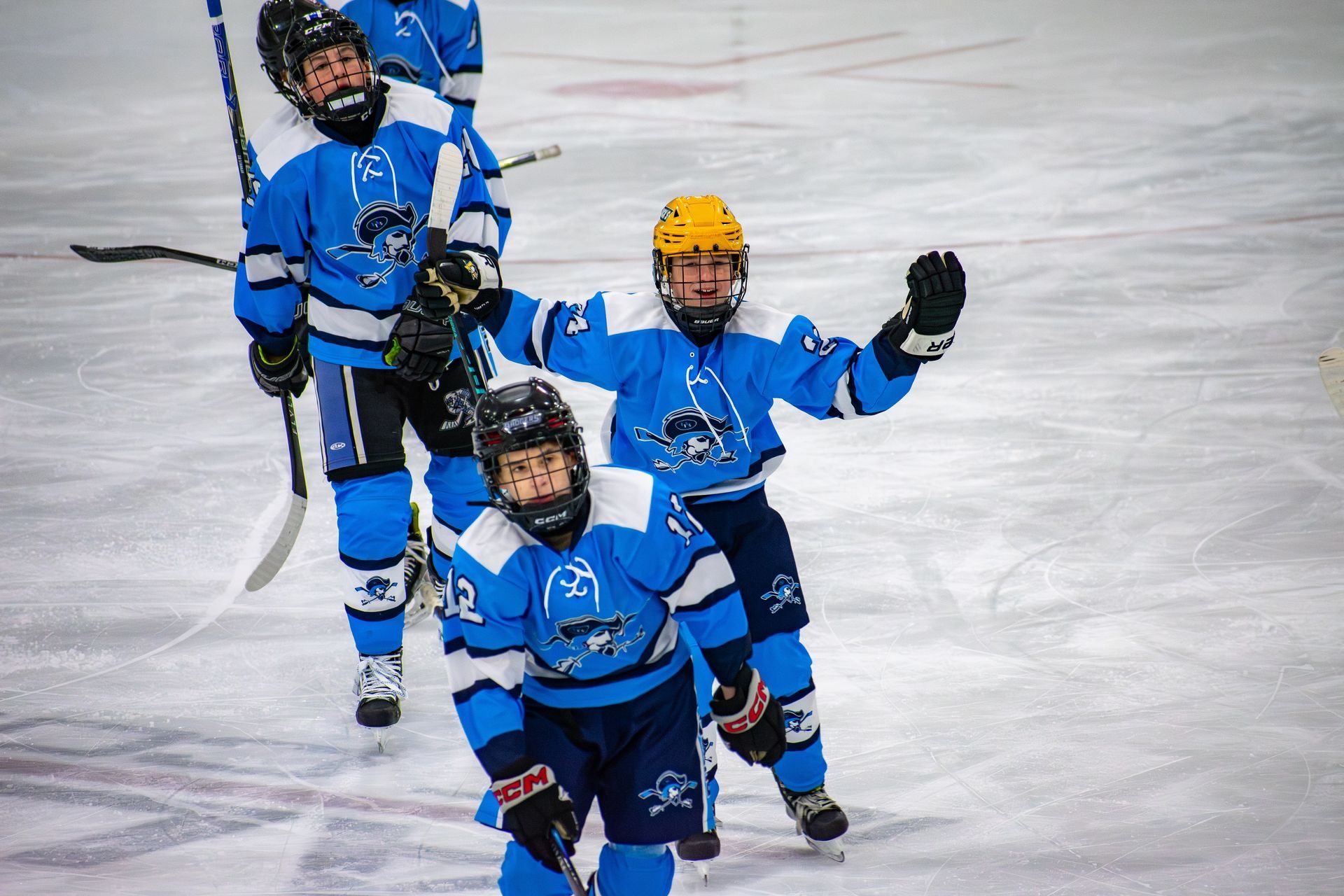 Three hockey players in bright blue uniforms celebrate on the ice, one with arms raised in victory.