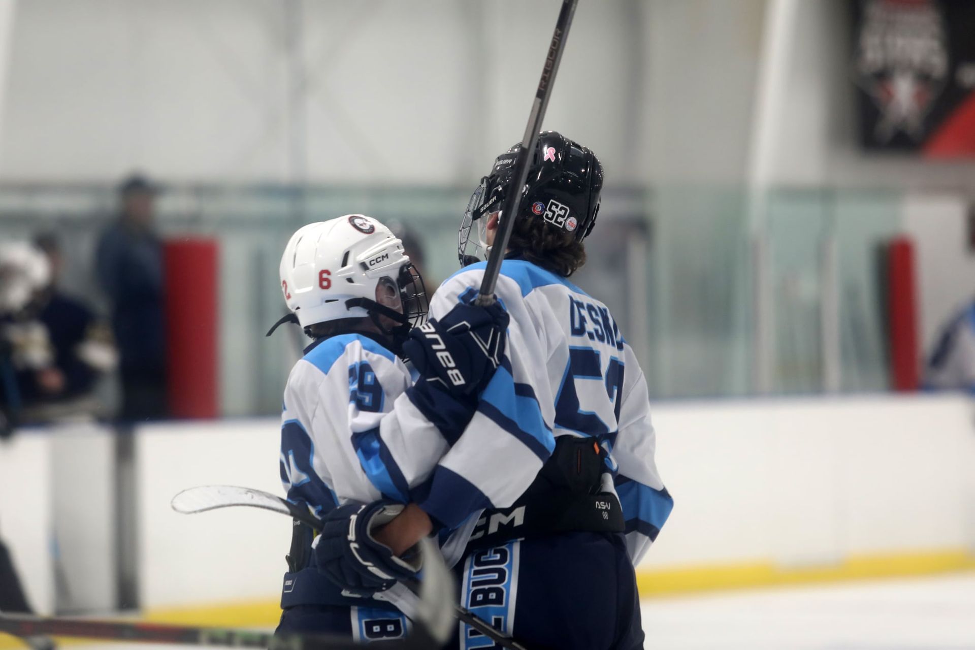 Two hockey players in white and blue uniforms hug and celebrate on the ice during a game.