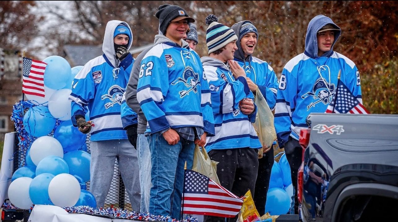 People wearing matching blue hockey jerseys and winter hats ride on a parade float decorated with blue and white balloons.