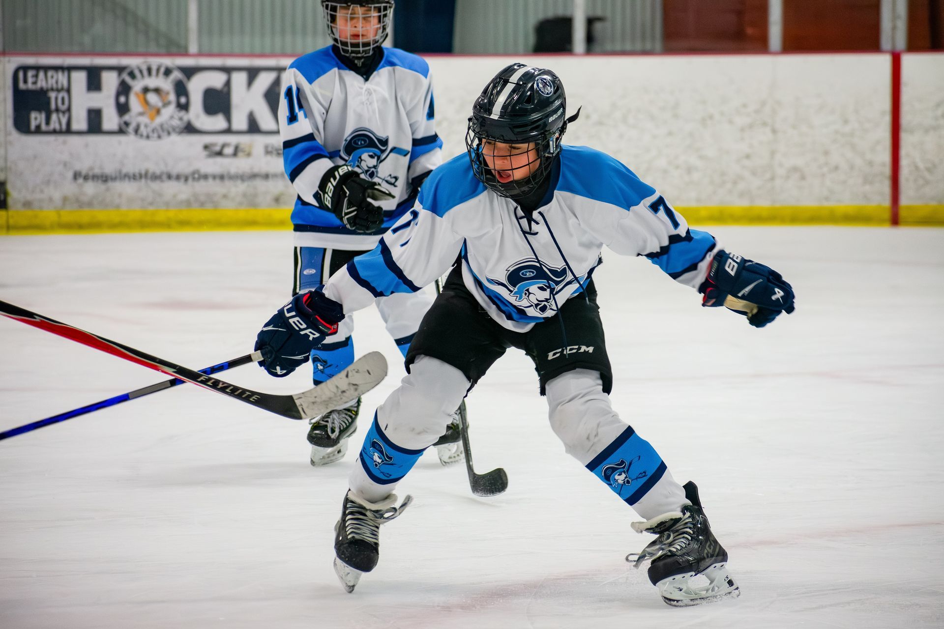 Two youth hockey players in blue and white jerseys practice on an ice rink.