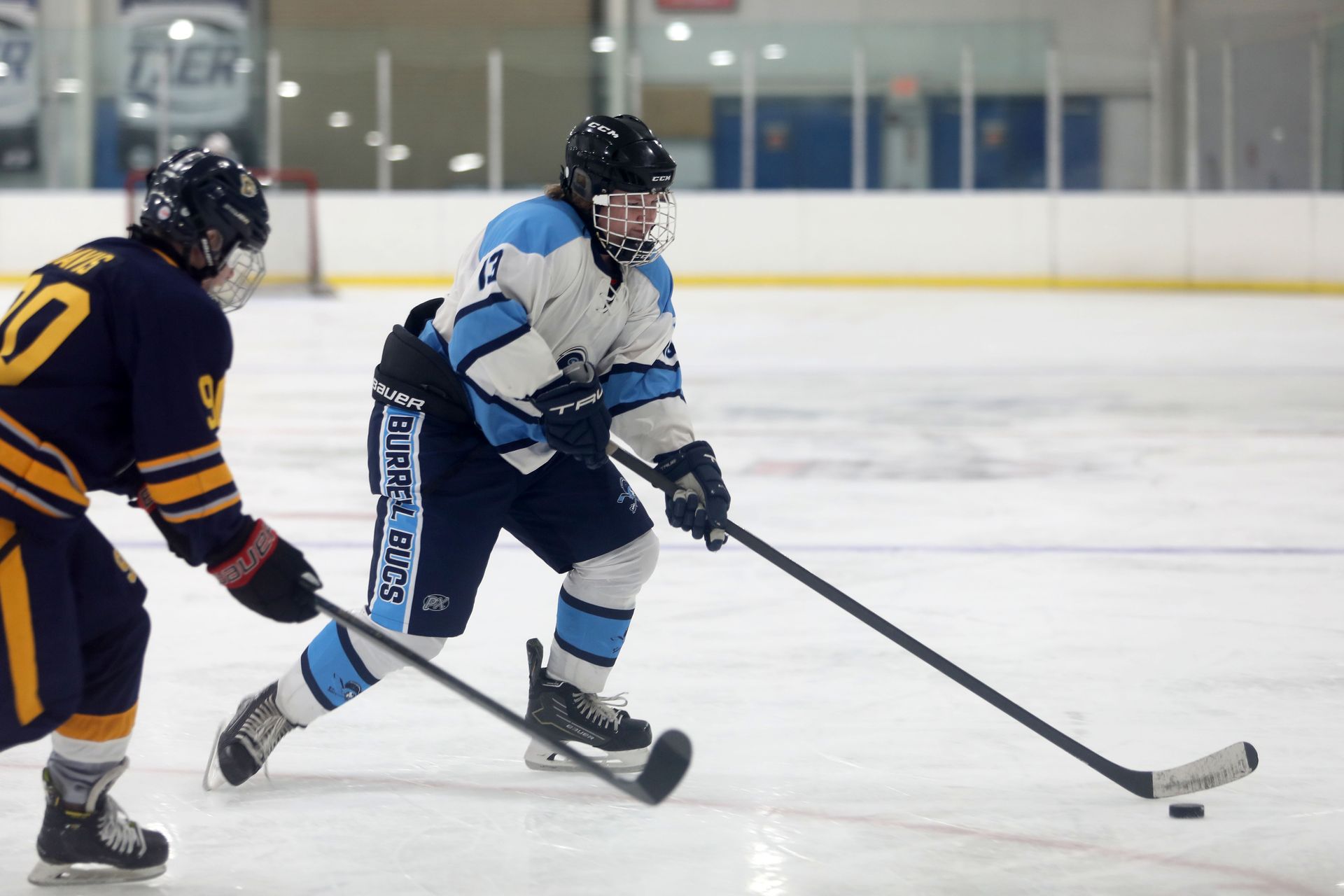 Two ice hockey players in team uniforms compete for the puck on an indoor ice rink.