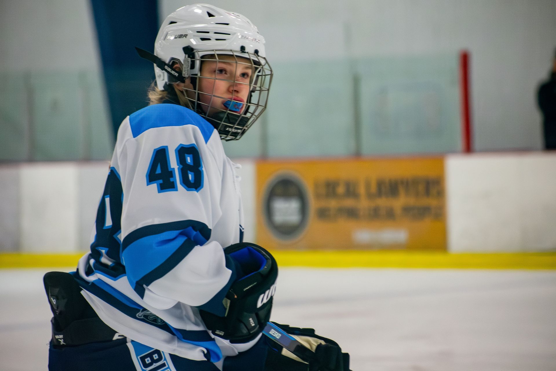 A hockey player in a white and blue uniform with the number 48 on their sleeve, wearing a helmet and looking on the ice.