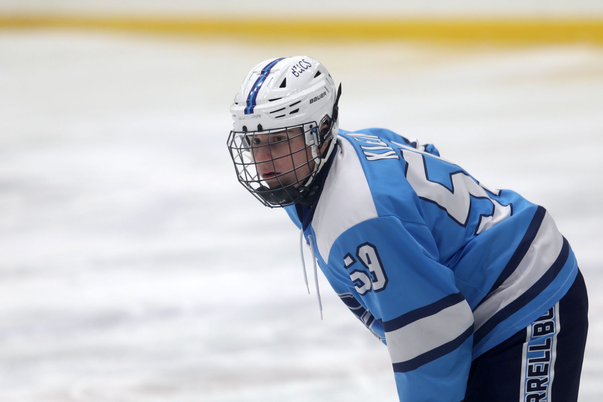A hockey player in a light blue and white jersey with number 59 stands on an ice rink, looking forward.